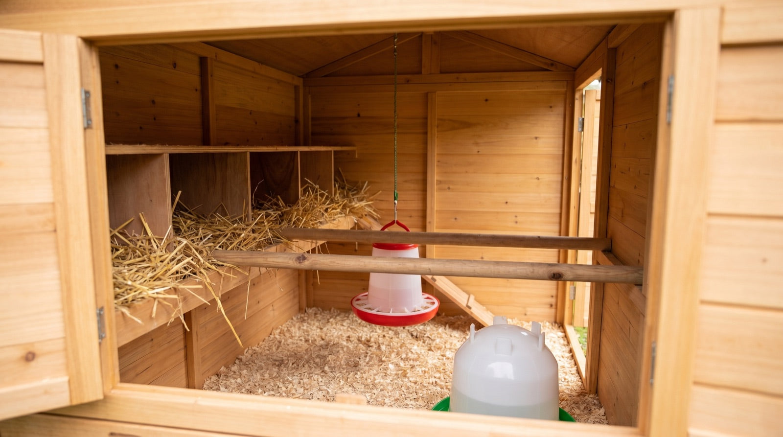 Interior of a wooden chicken coop with nest boxes, perch, feeder and drinker